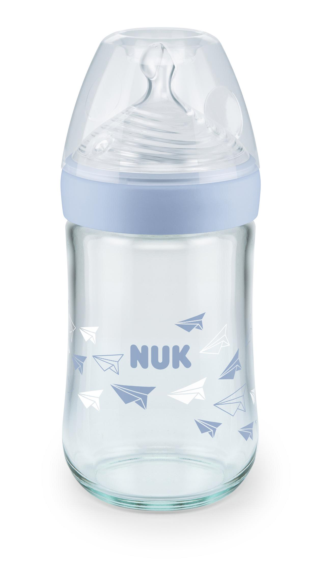 Eine durchsichtige Nuk-Babyflasche mit blauem Ring und Papierfliegermotiv.