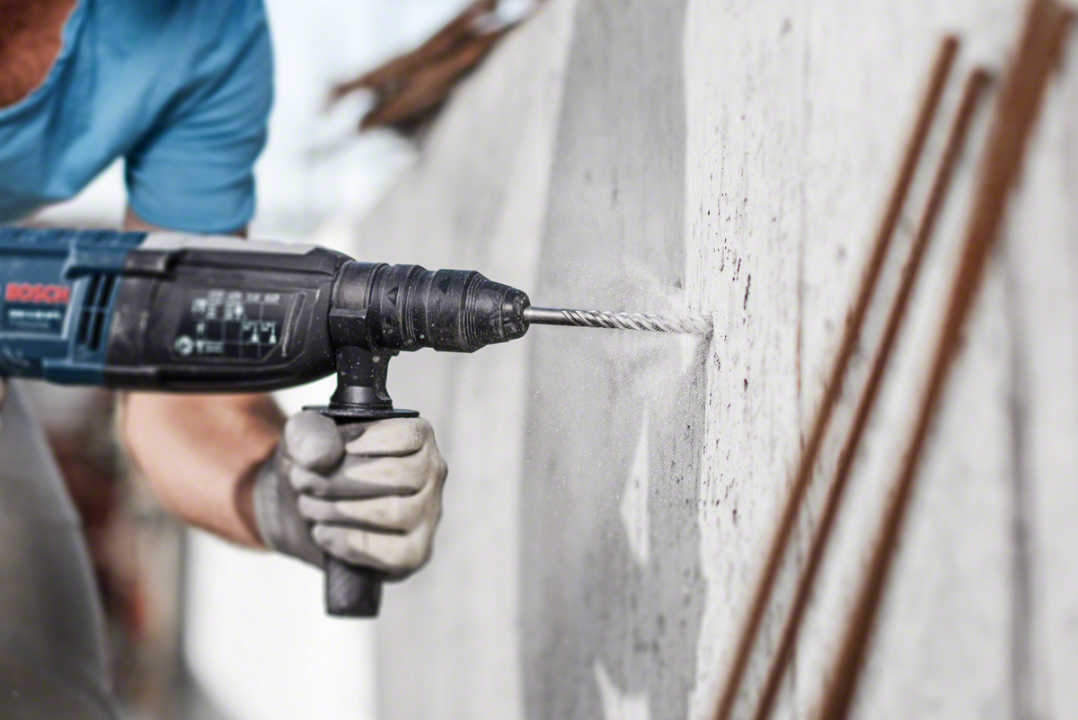 Behandschuhte Hand bohrt Betonwand. Blaue Bosch-Bohrmaschine, Staub fliegt.