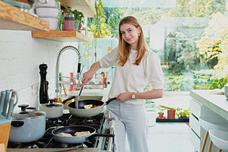 A woman cooks in a kitchen with stovetop pans and ingredients.