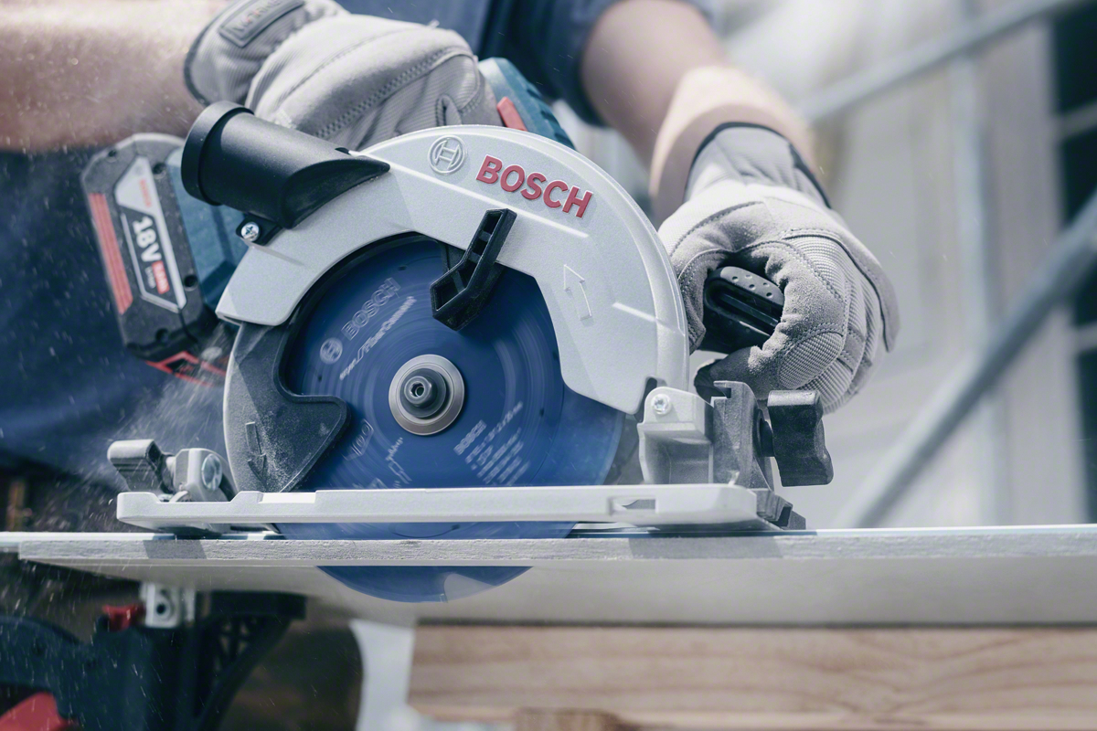 Eine Hand mit Handschuh bedient eine Bosch-Kreissäge, die Holz schneidet.