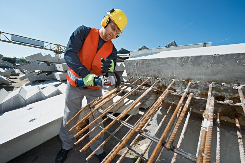 Mann mit Winkelschleifer bearbeitet Bewehrungsstahl auf Baustelle.