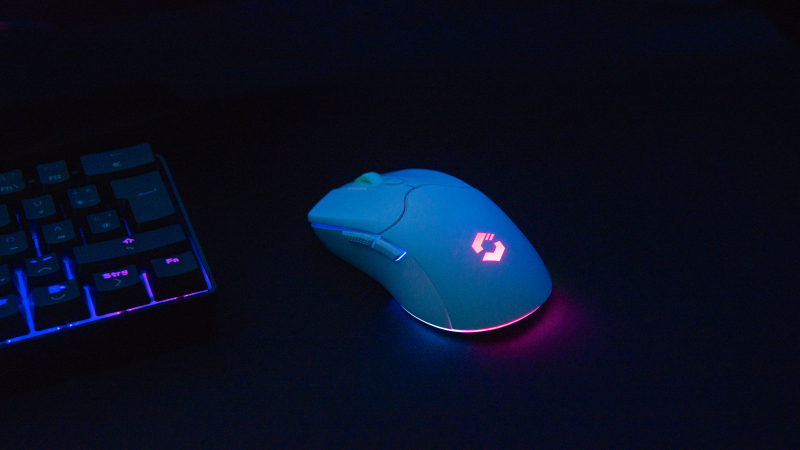 Eine weiße Gaming-Maus mit rotem Logo neben einer schwarzen Tastatur mit blauer und pinker Hintergrundbeleuchtung.