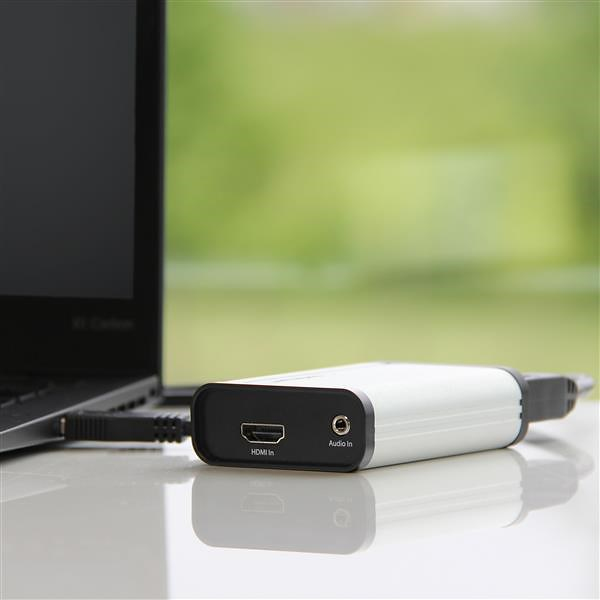 Portátil conectado a un dispositivo de captura blanco con puertos HDMI y audio.