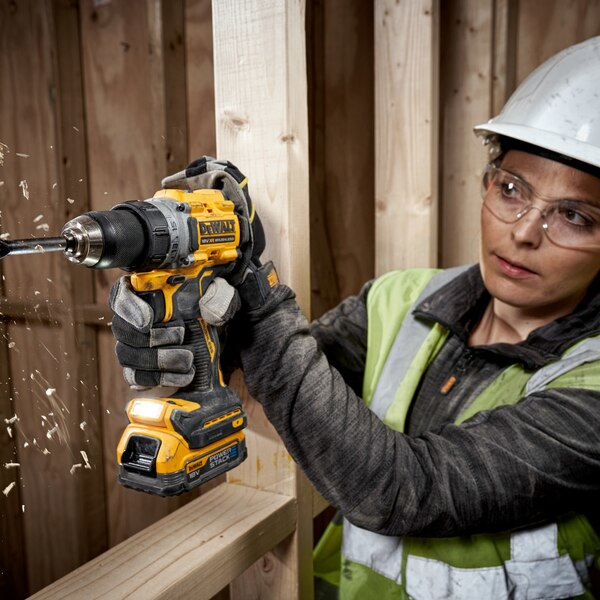 Frau mit Helm bohrt mit gelber Bohrmaschine in Holz. Holzspäne fliegen.