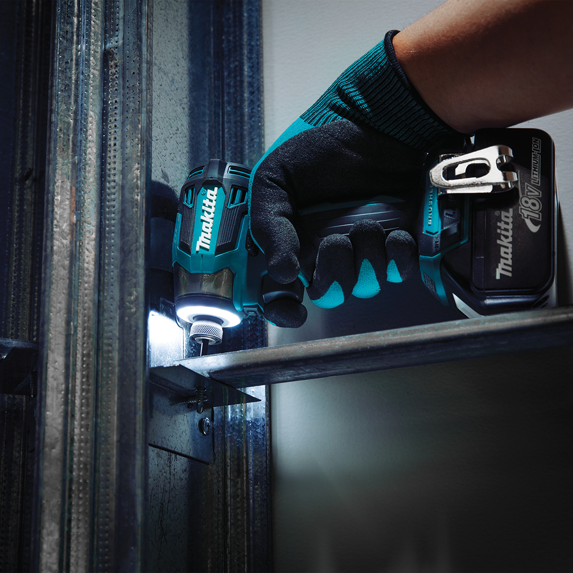 Mano guantata usa avvitatore a percussione Makita su telaio metallico.