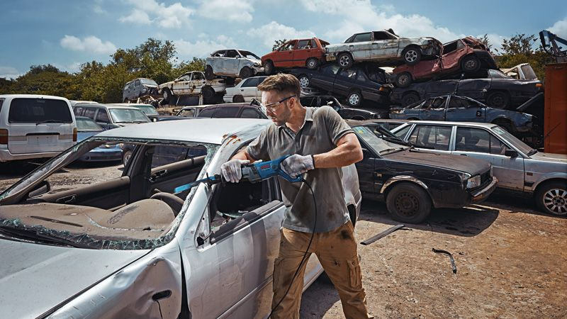 Un uomo smantella un rottame d'auto con un attrezzo in una discarica.