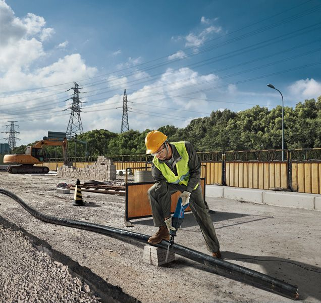 Operaio con casco e gilet usa elettroutensile su cavo spesso in cantiere.