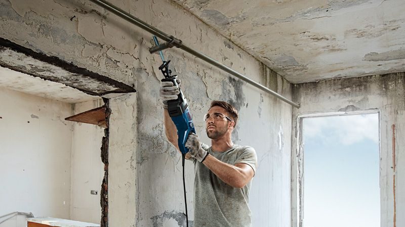 Un uomo con occhiali e guanti usa un seghetto alternativo su un tubo.