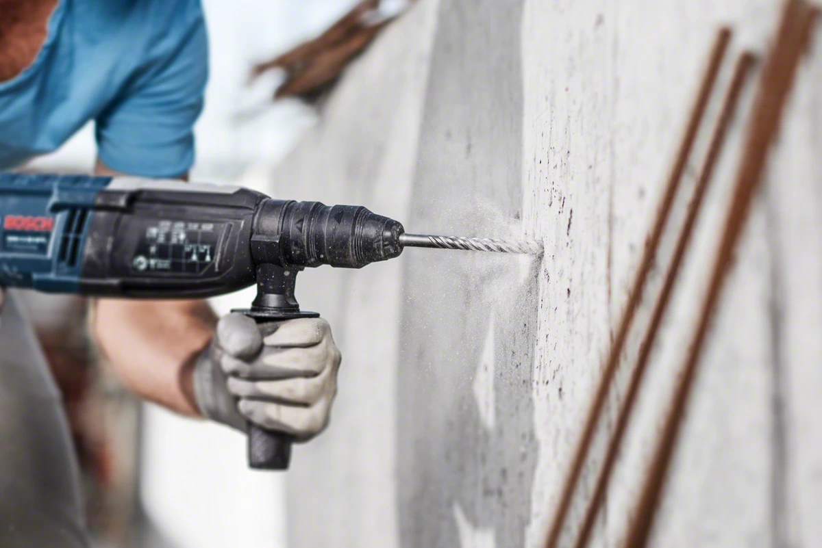 Hand bohrt mit Schlagbohrmaschine in Betonwand. Staub wirbelt auf.