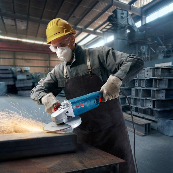 Kasklı ve maskeli bir işçi metal zımparalıyor. Kıvılcımlar uçuşuyor.