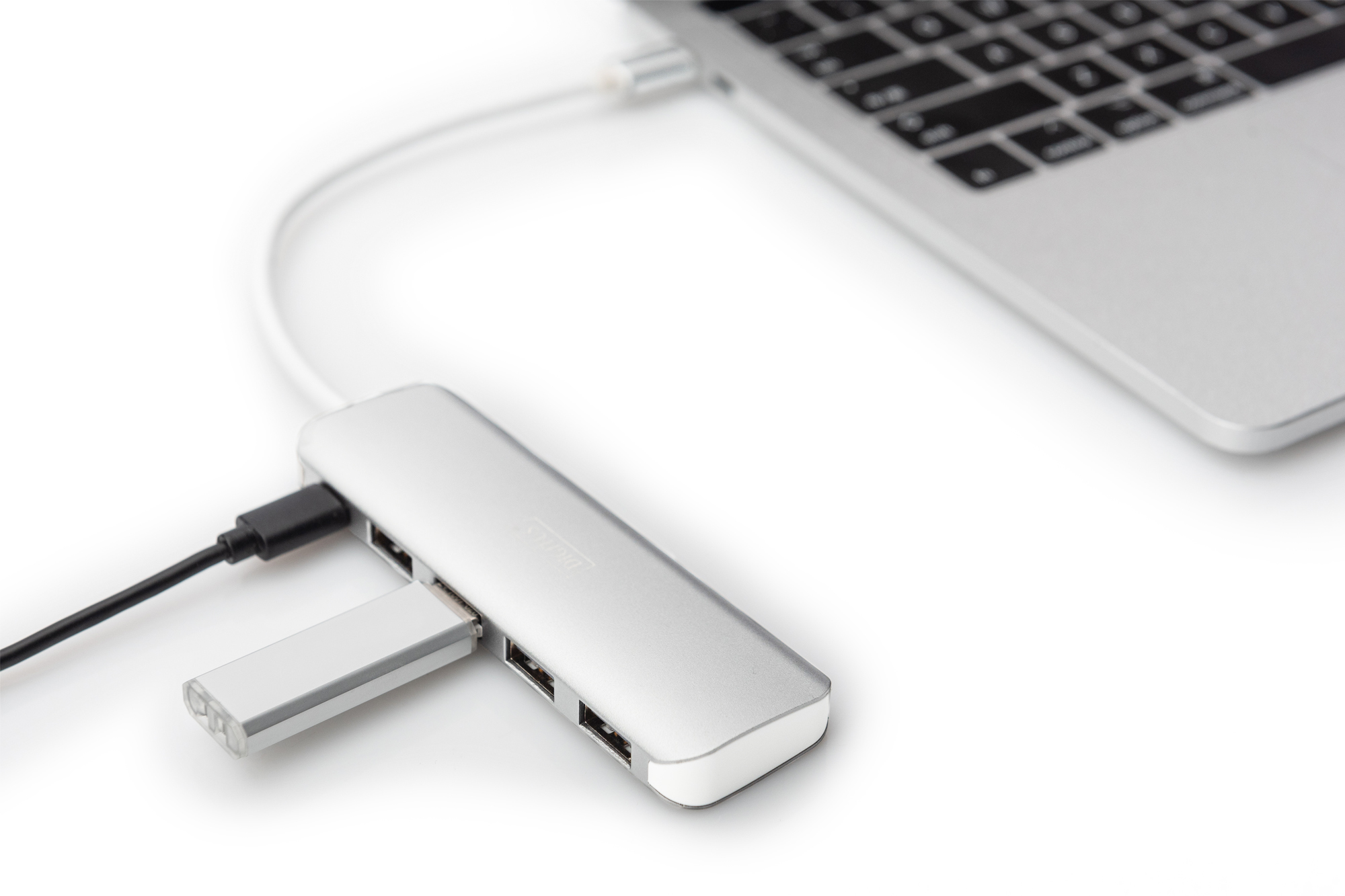 Silberner USB-C-Hub mit angeschlossenen Kabeln und einem USB-Stick, neben einem Laptop.