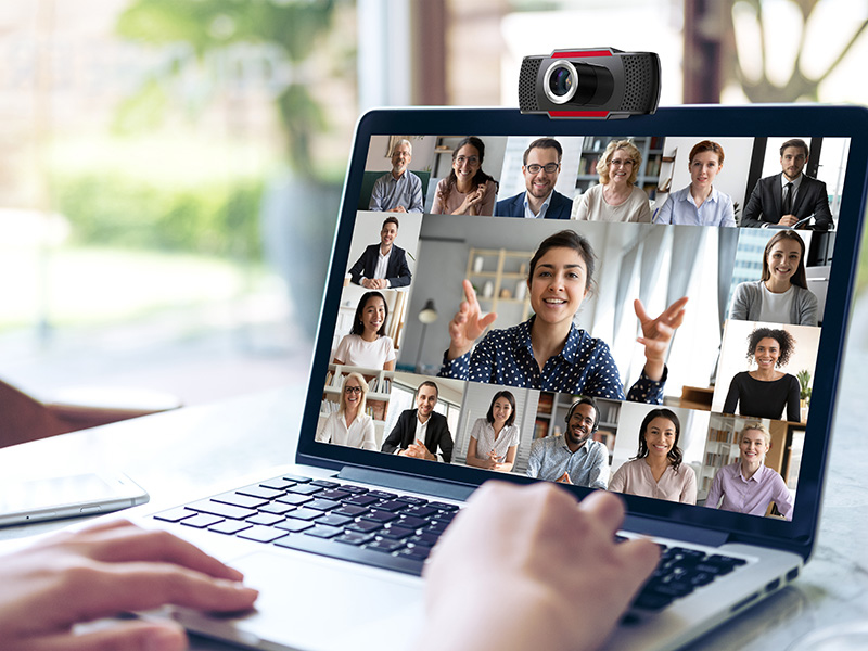Schermo del laptop mostra una videoconferenza con più partecipanti. Una webcam è in alto.