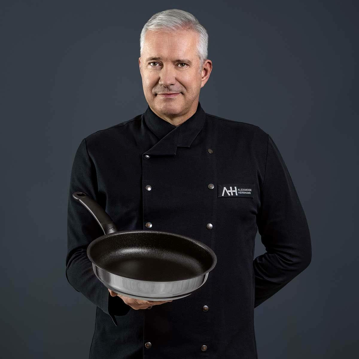 Un uomo in giacca da chef nera tiene una padella.