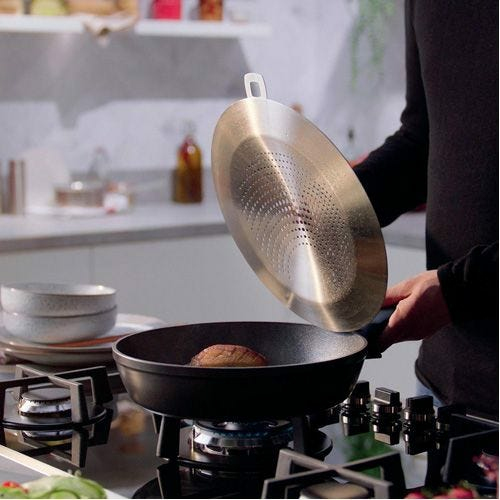 Un pezzo di carne frigge in una padella su un fornello a gas, con un paraspruzzi sollevato.