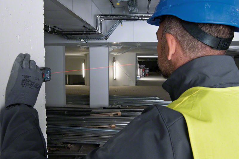 Bauarbeiter misst mit Laserentfernungsmesser an einer Wand in einer Baustelle.