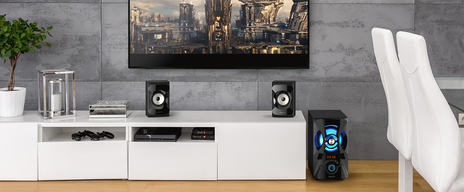 Una sala de estar con TV, altavoces, consola y mueble blanco.