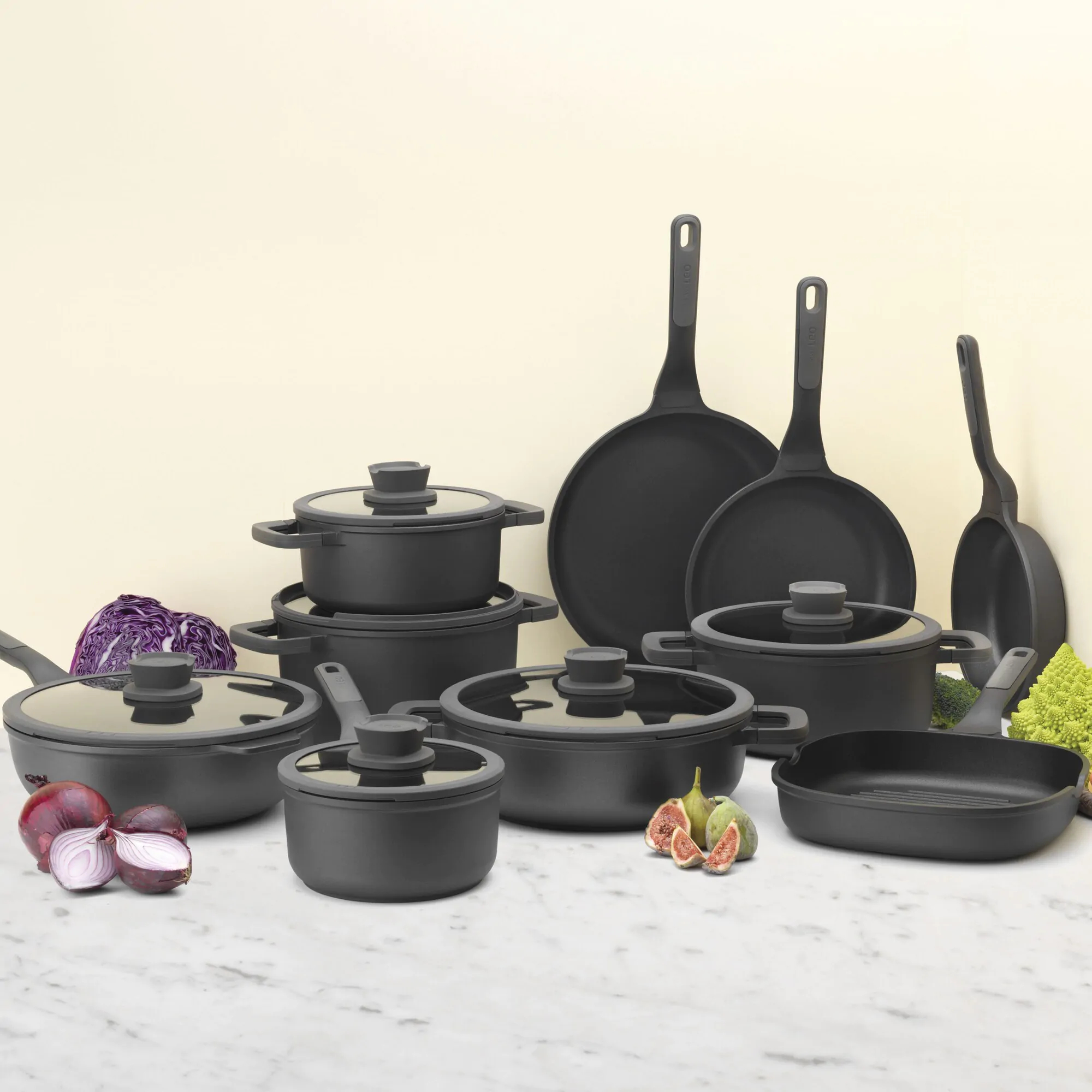 Black cookware set with vegetables like red cabbage, broccoli, and figs.