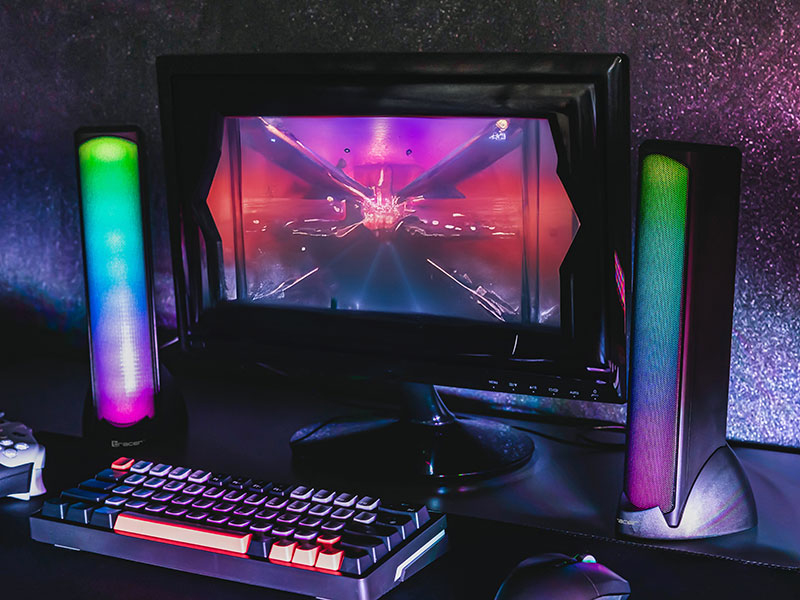 Ein Gaming-Setup mit Monitor, Tastatur, Maus und zwei beleuchteten Lautsprechern.