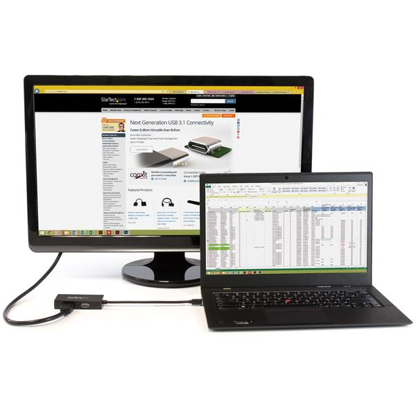 Un monitor grande muestra una página web, un portátil una hoja de cálculo. Un adaptador USB los conecta.
