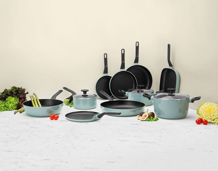 Light blue cookware with black handles on marble counter with vegetables.
