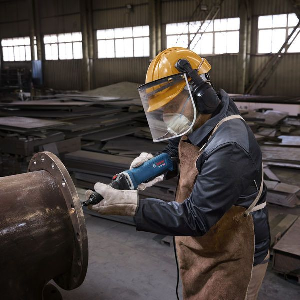 Güvenlik teçhizatlı adam atölyede taşlama makinesiyle metal boru zımparalıyor.