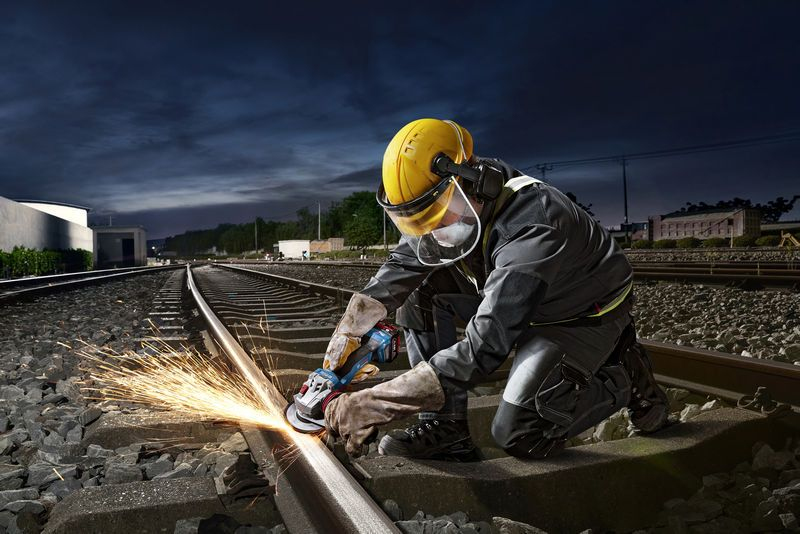 Ein Arbeiter schleift eine Bahnschiene bei Nacht, Funken fliegen.