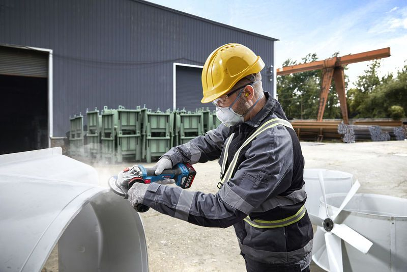 Mann mit Schutzhelm schleift große weiße Form mit Winkelschleifer im Freien.