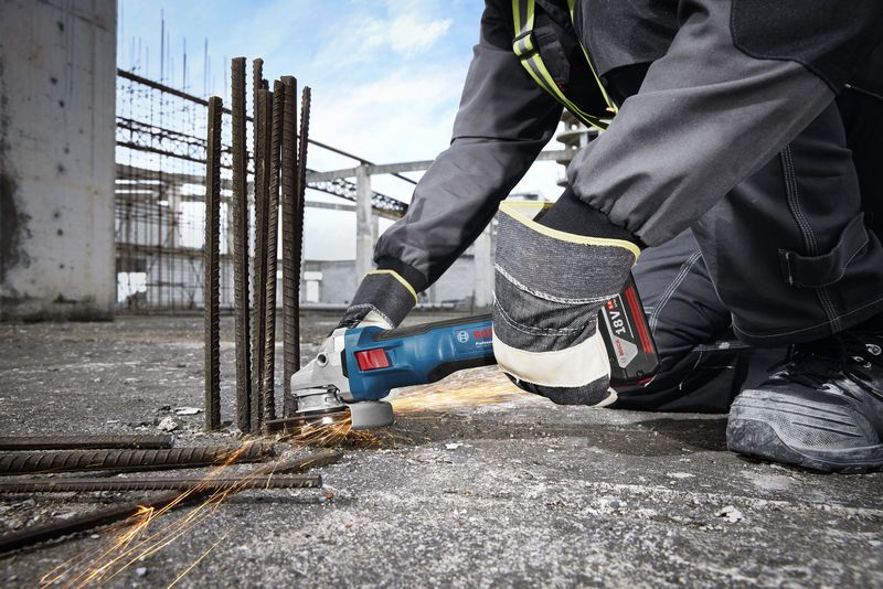Ein Bauarbeiter schleift mit einem Winkelschleifer Metallstäbe auf einer Baustelle.