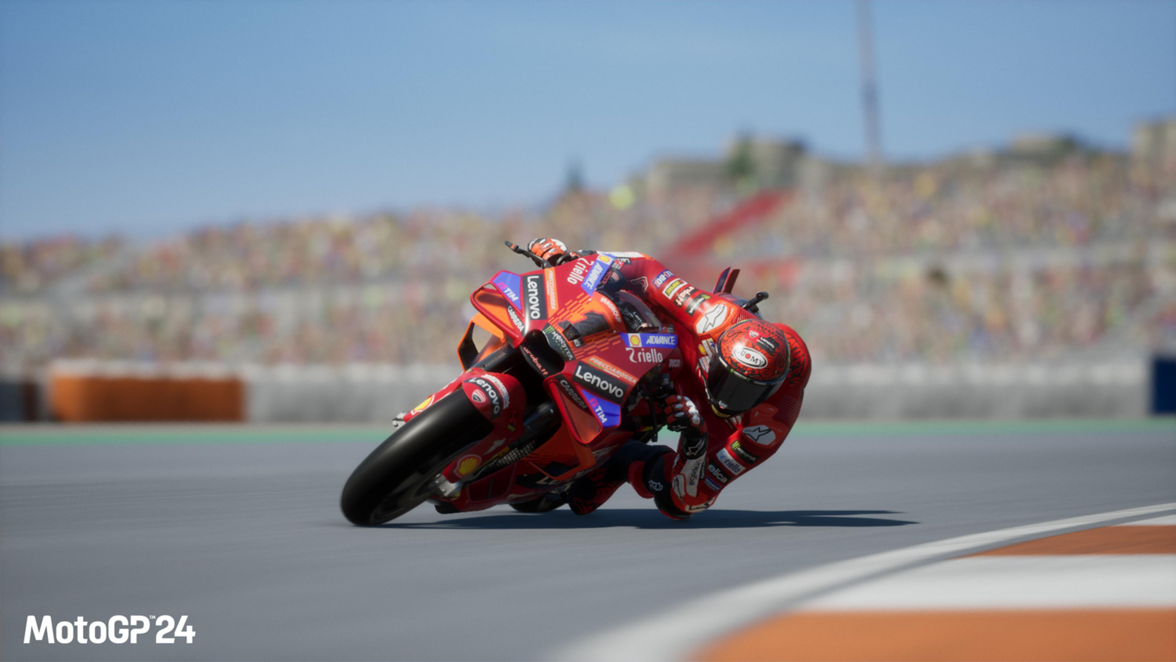 Un pilota MotoGP rosso in piega su una pista da corsa con tribune sullo sfondo.