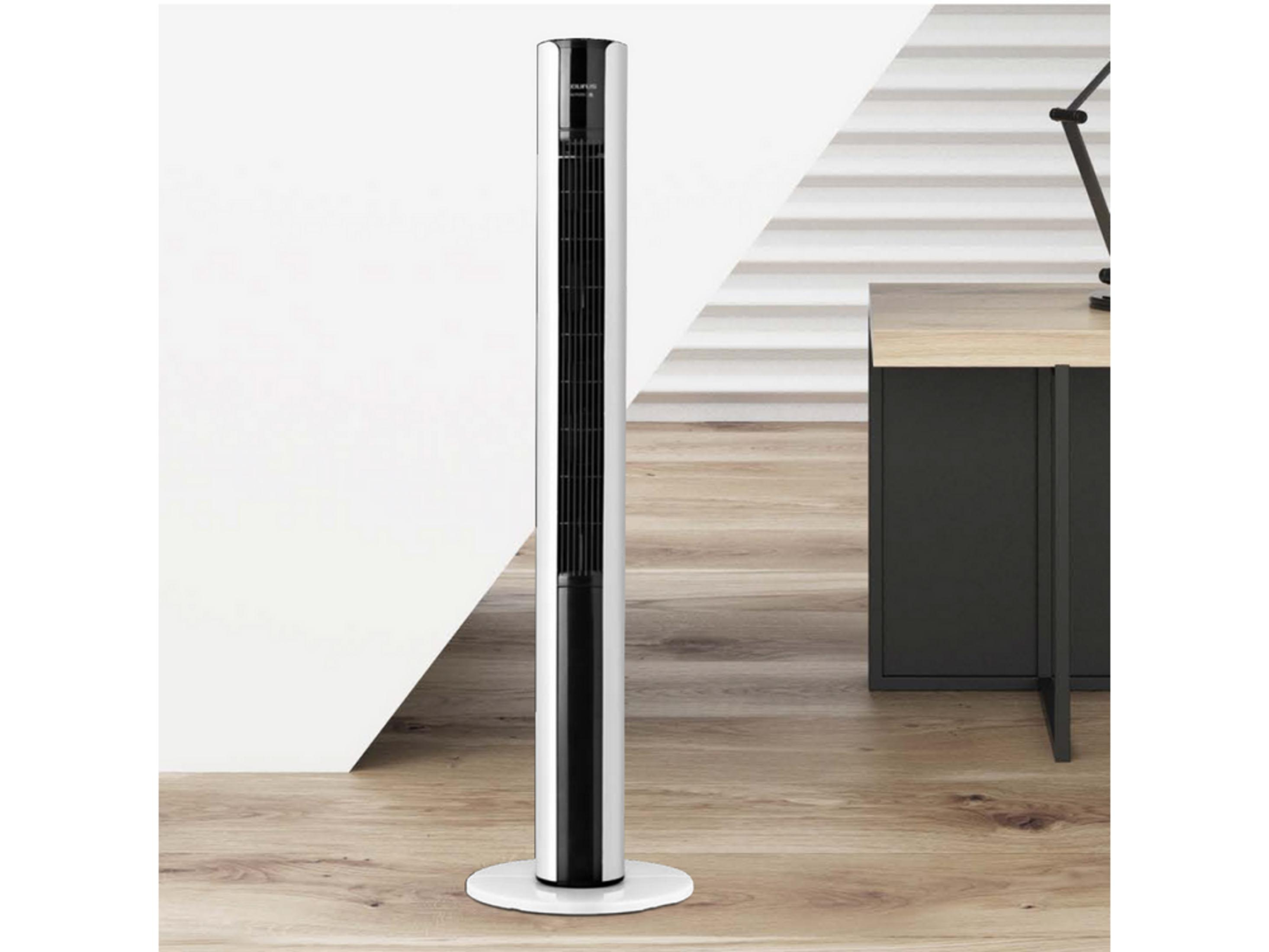 Ein schlanker, weißer Turmventilator steht auf einem Holzboden neben einem Schreibtisch.