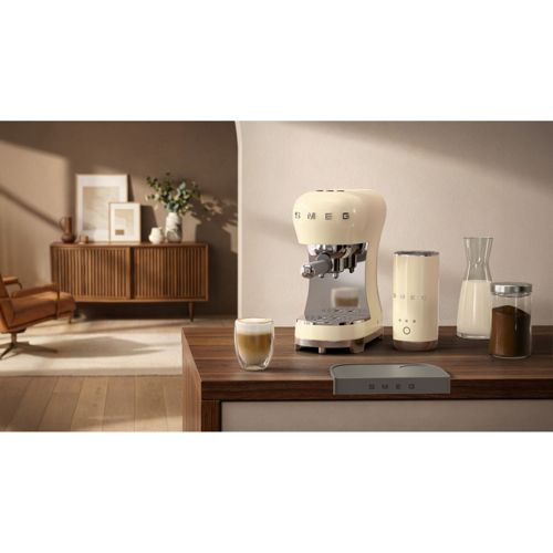 Cremefarbene SMEG Espressomaschine mit Milchaufschäumer, Glas und Bohnen.
