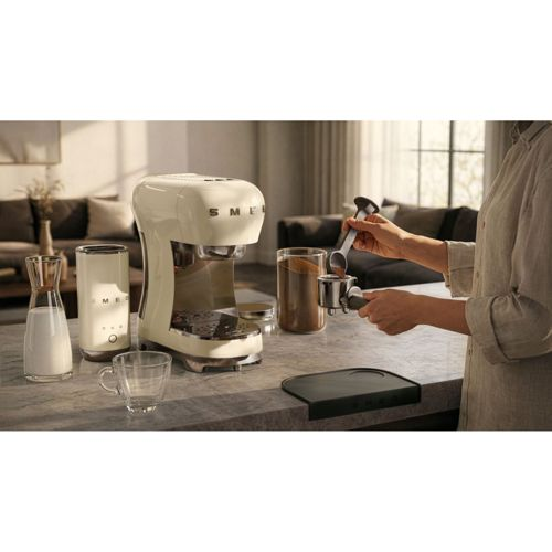 Eine Person bereitet Kaffee mit einer weißen Espressomaschine zu. Ein Glas Milch steht daneben.