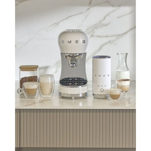 Ein cremefarbener Smeg-Kaffeevollautomat mit Zubehör, darunter Kaffeetassen und ein Milchaufschäumer.
