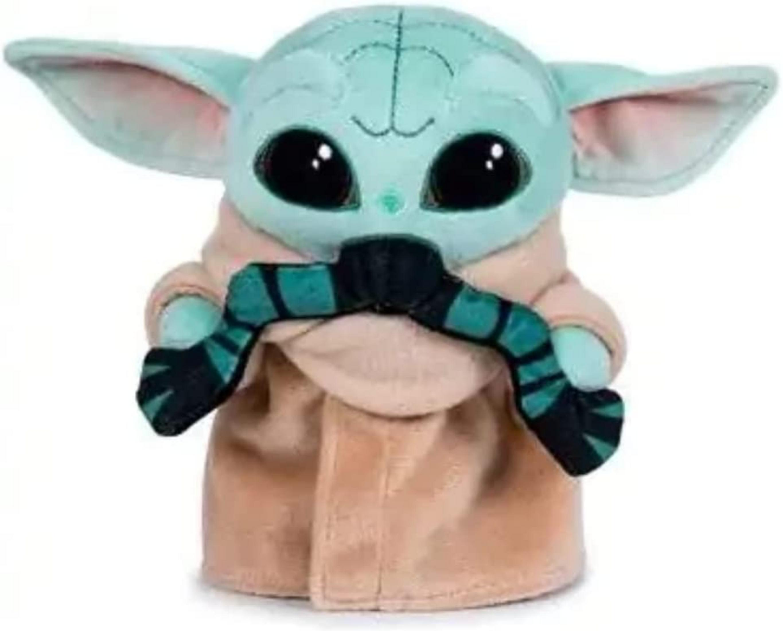 Un peluche de Baby Yoda con túnica color canela sostiene un objeto verde y negro.