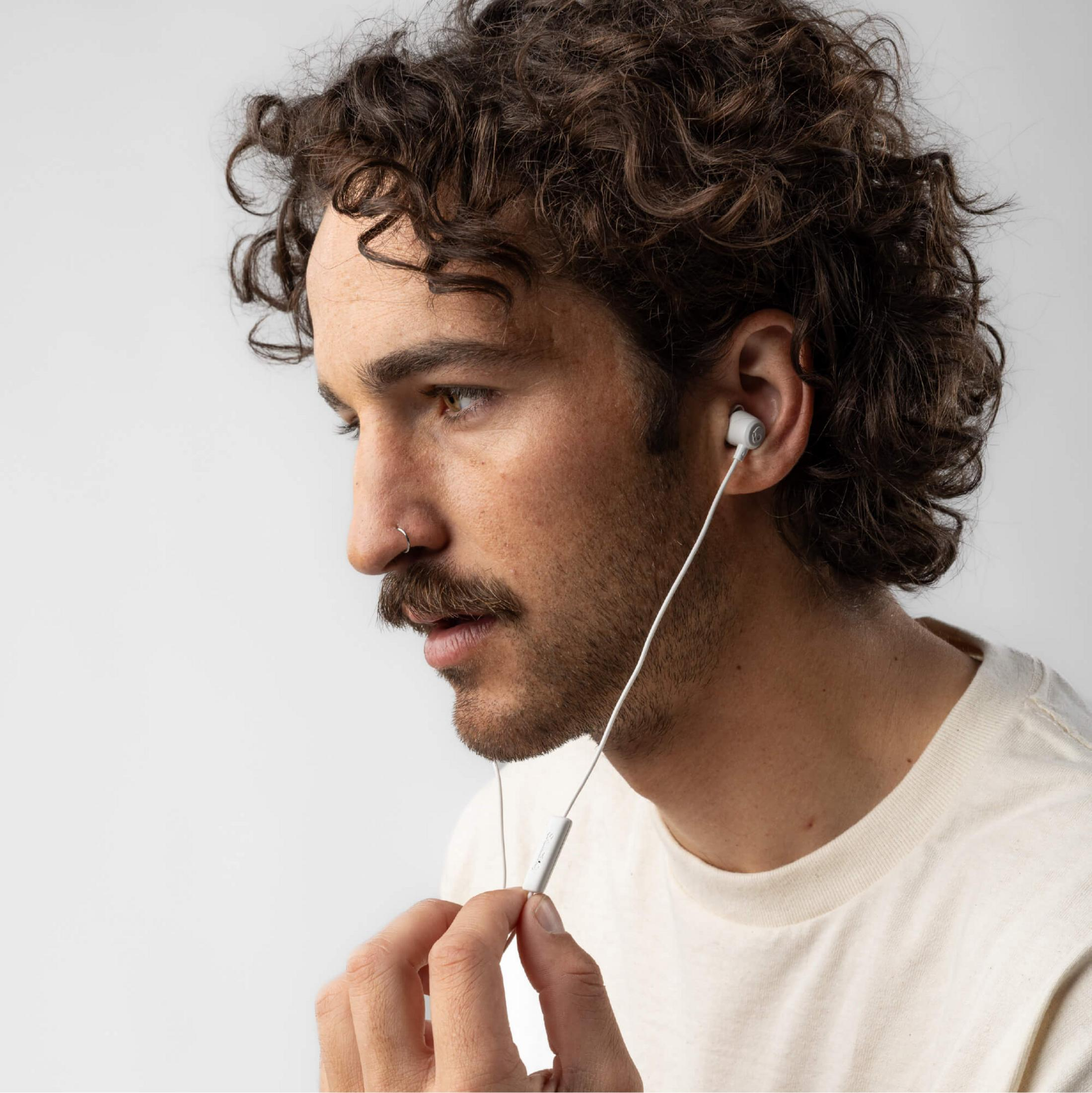 Mann mit Locken, Schnurrbart, Nasenring und Ohrhörern, der ein weißes Hemd trägt.