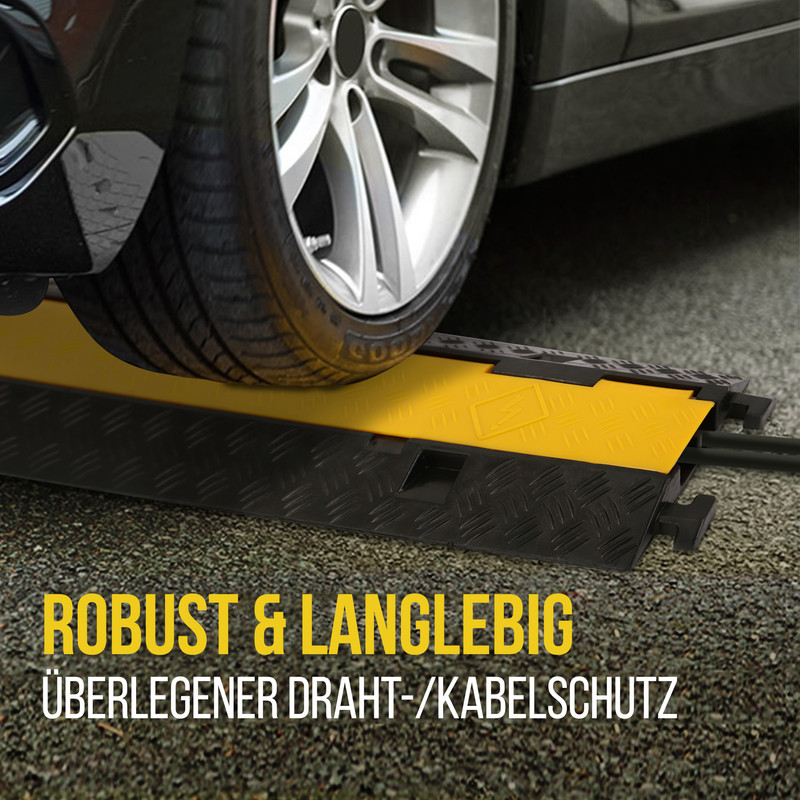 Ein Autoreifen fährt über einen gelben Kabelschutz auf Asphalt.