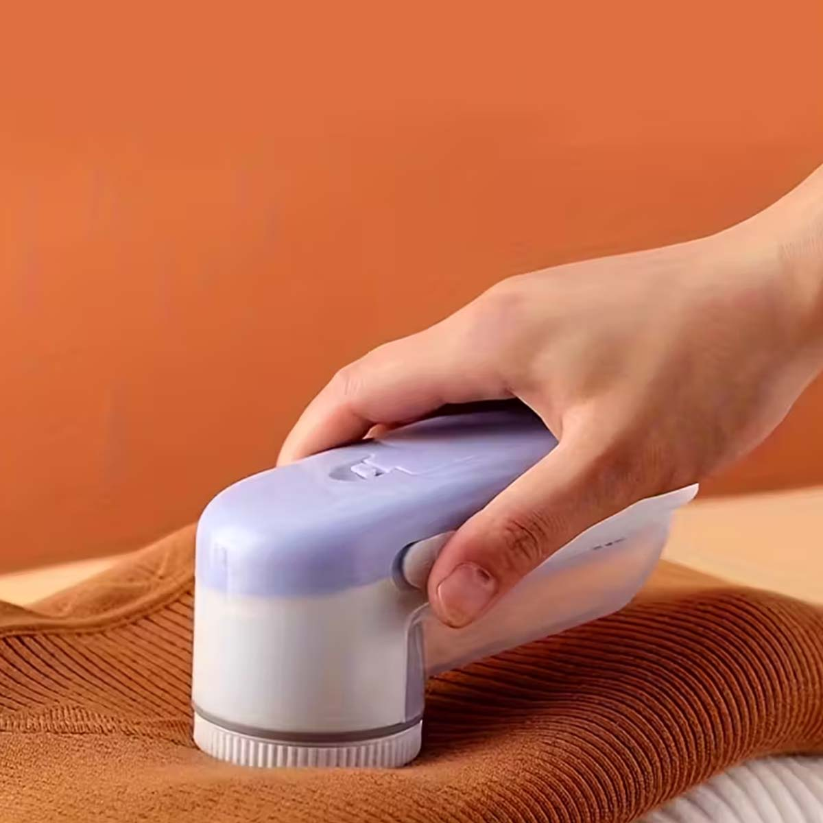Eine Hand hält einen Fusselentferner über einem braunen Pullover.