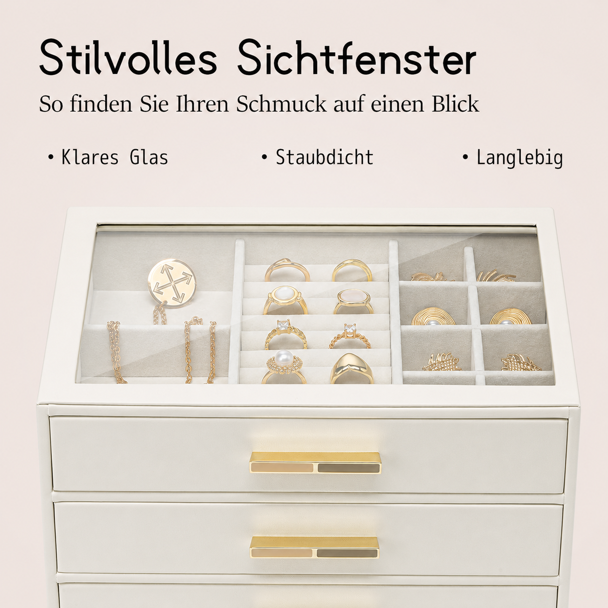 Ein weißer Schmuckkasten mit Glashaube zeigt Ringe, Ketten und Broschen. Drei Schubladen.