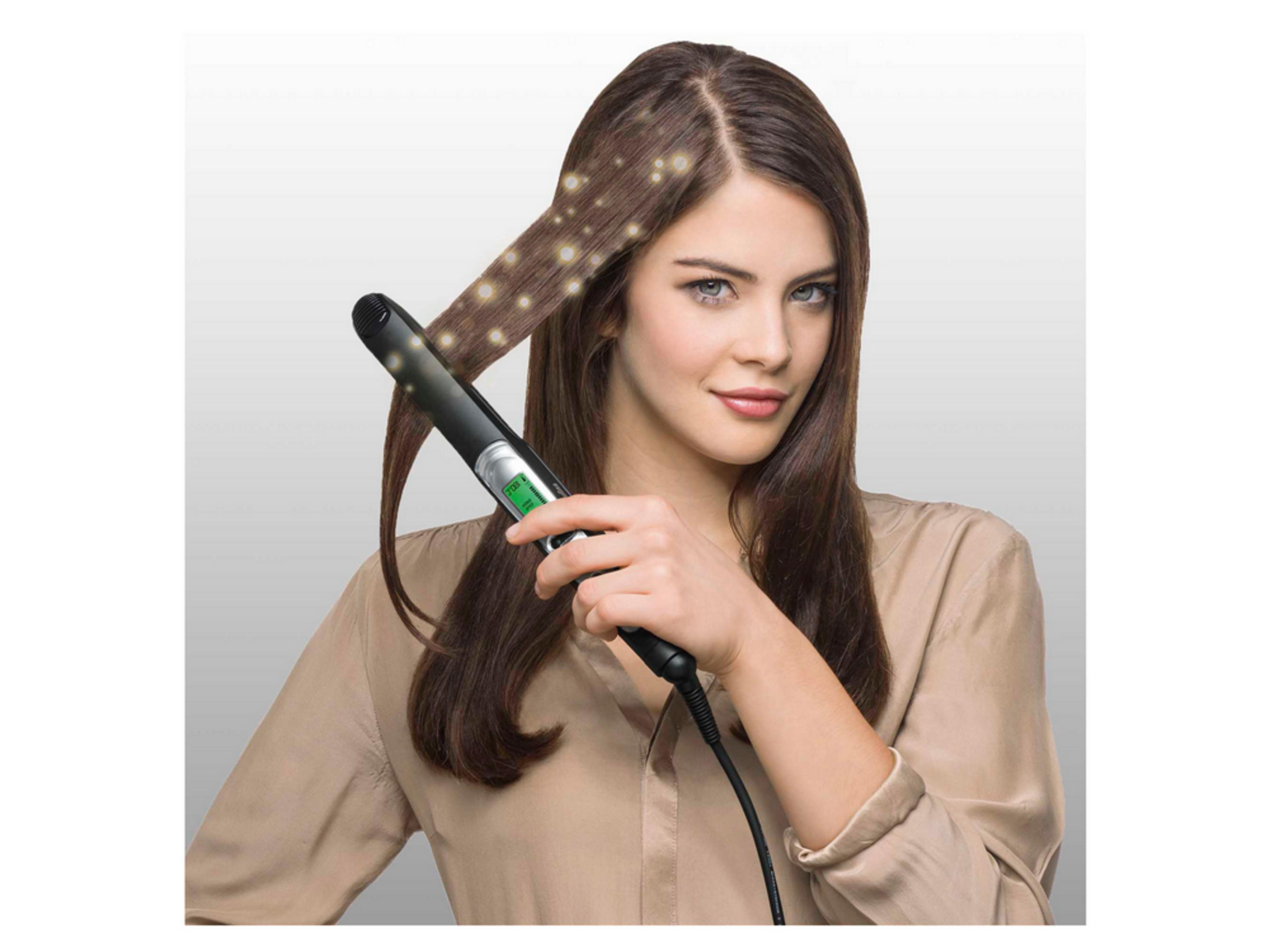 Una donna si liscia i capelli castani con una piastra nera adornata di luci.