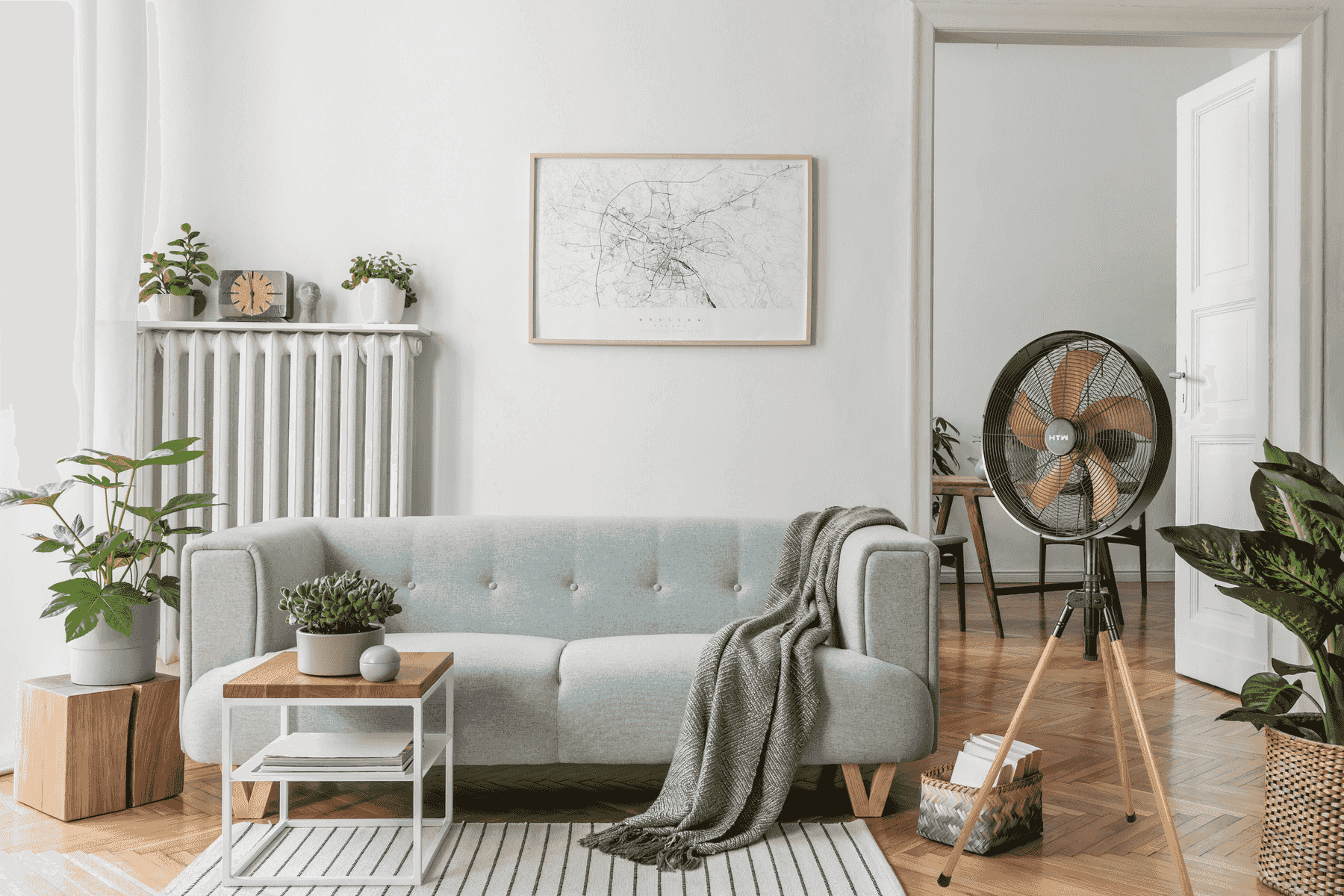 Una sala de estar luminosa con sofá, mesa, plantas y ventilador.