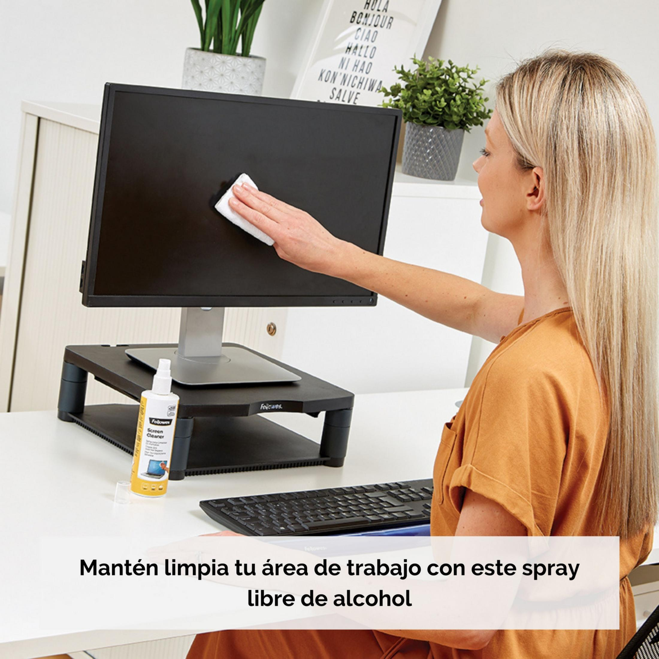 Una donna pulisce lo schermo di un monitor con un panno. Vicino c'è una bottiglia di detergente.
