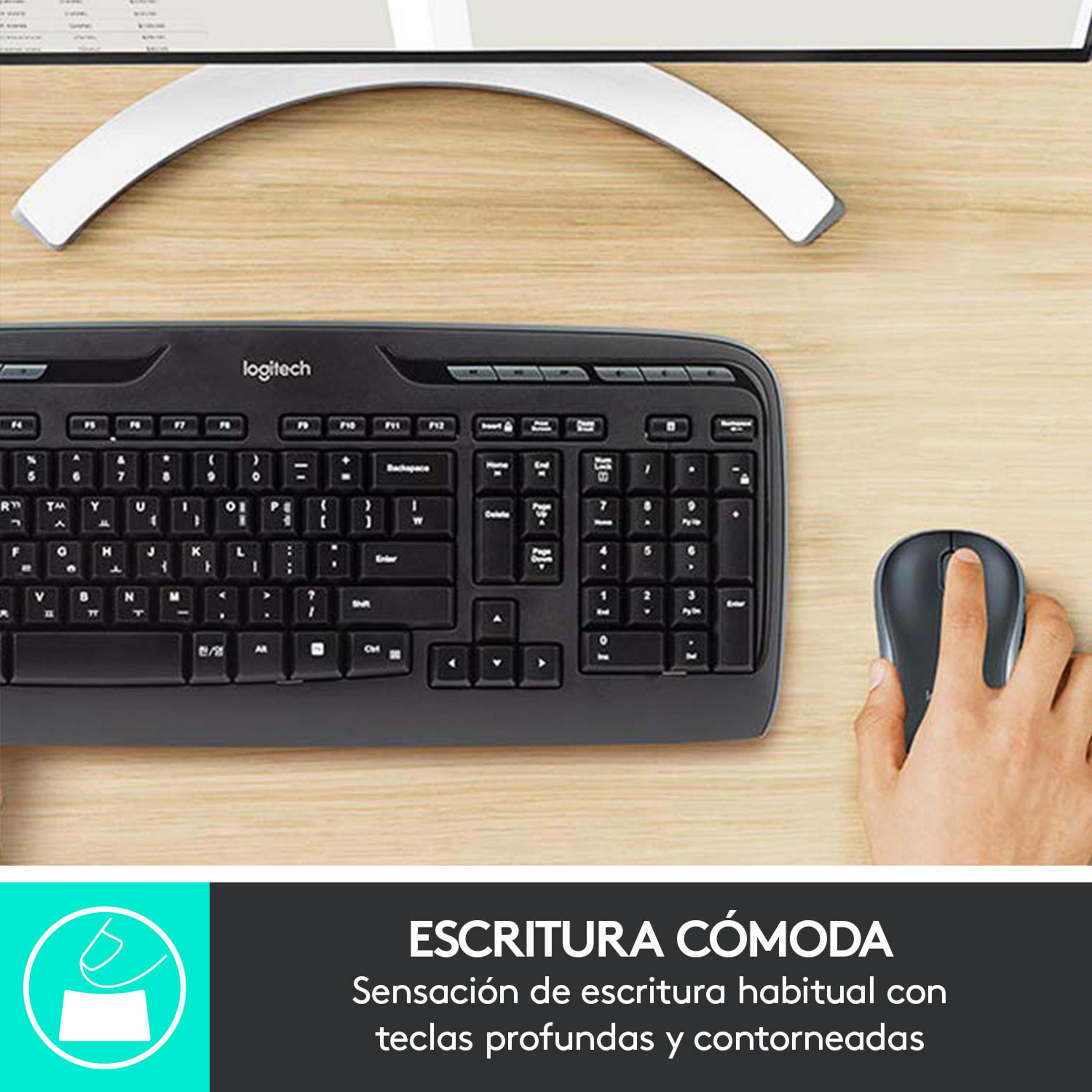Una mano usa un mouse Logitech accanto a una tastiera nera su una scrivania di legno.