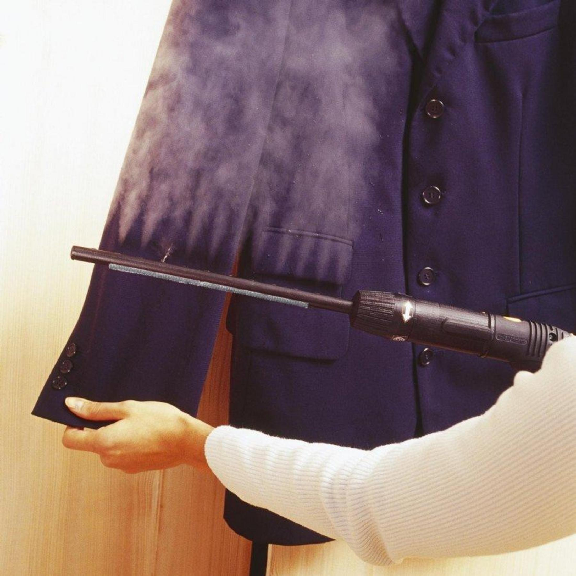 Una persona stira un abito blu navy con un ferro da stiro a vapore, creando vapore.