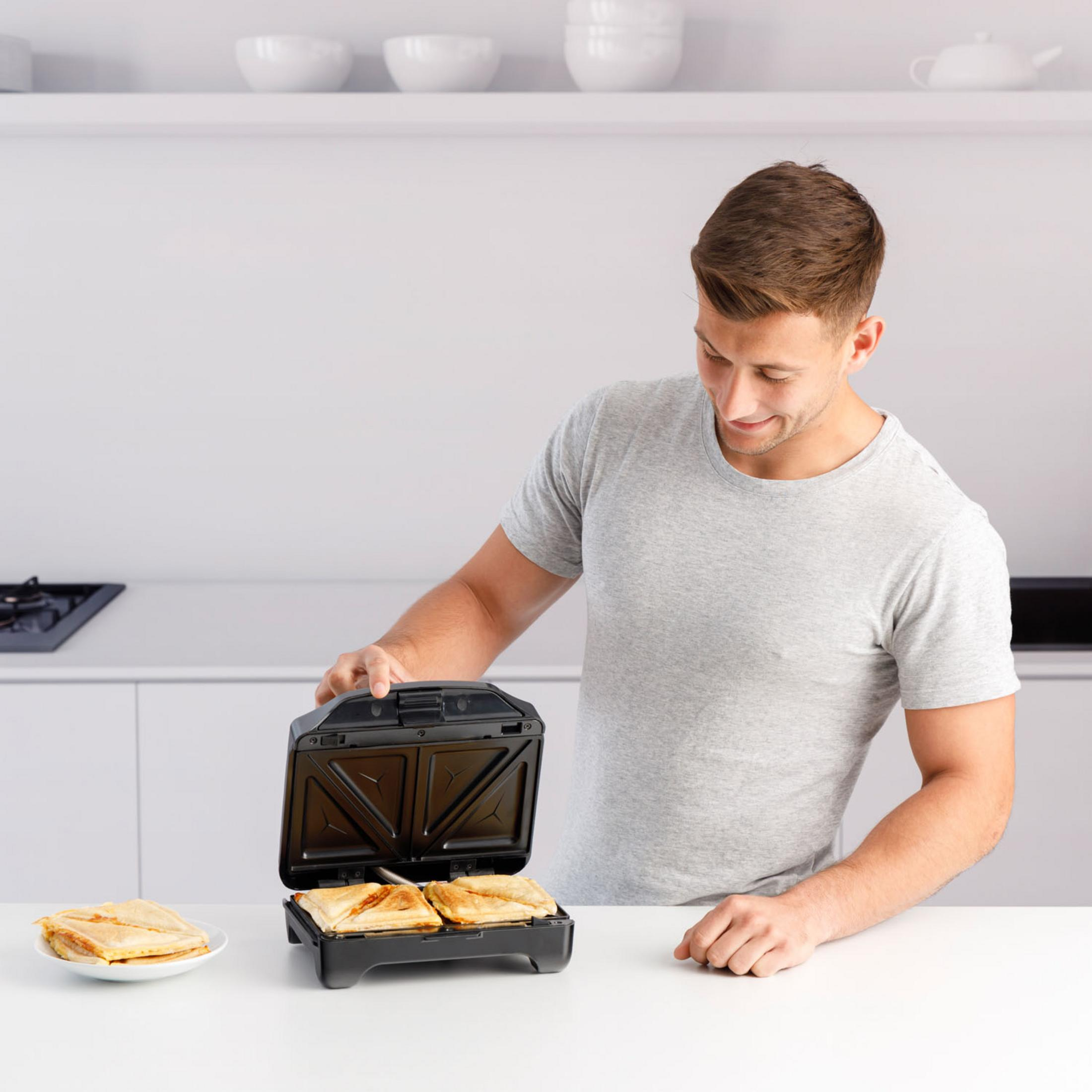 Uomo in maglietta grigia usa piastra per toast. Toast su piatto.