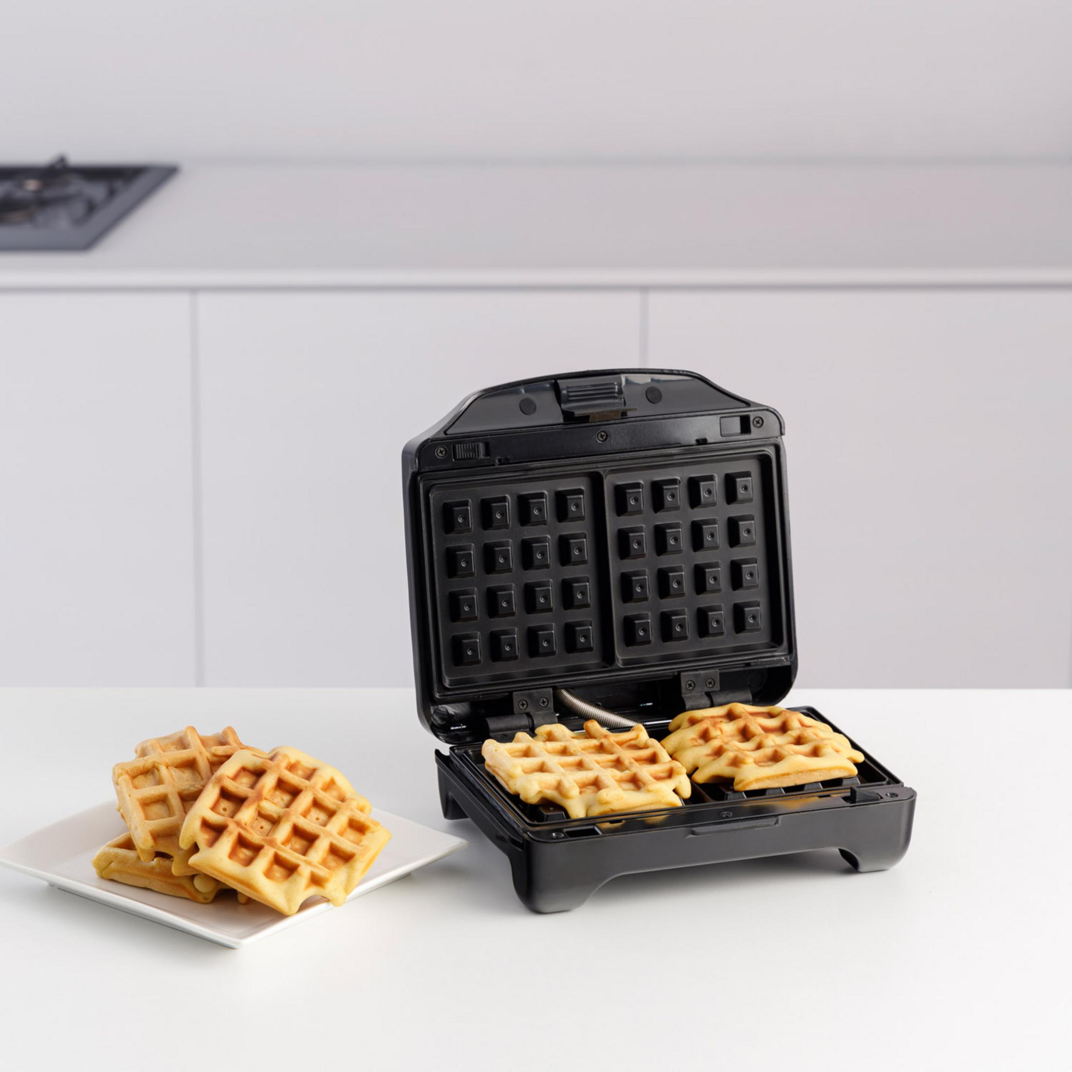 Una piastra per waffle aperta con tre waffle, due nella piastra e uno su un piatto.