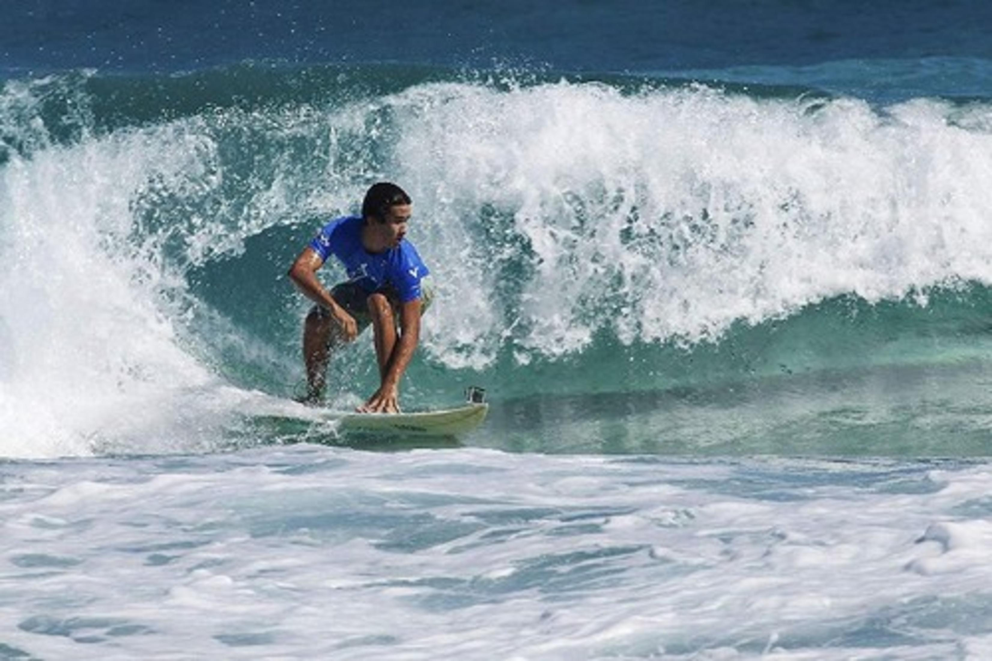 Un surfista con camiseta azul surfea una ola rota.