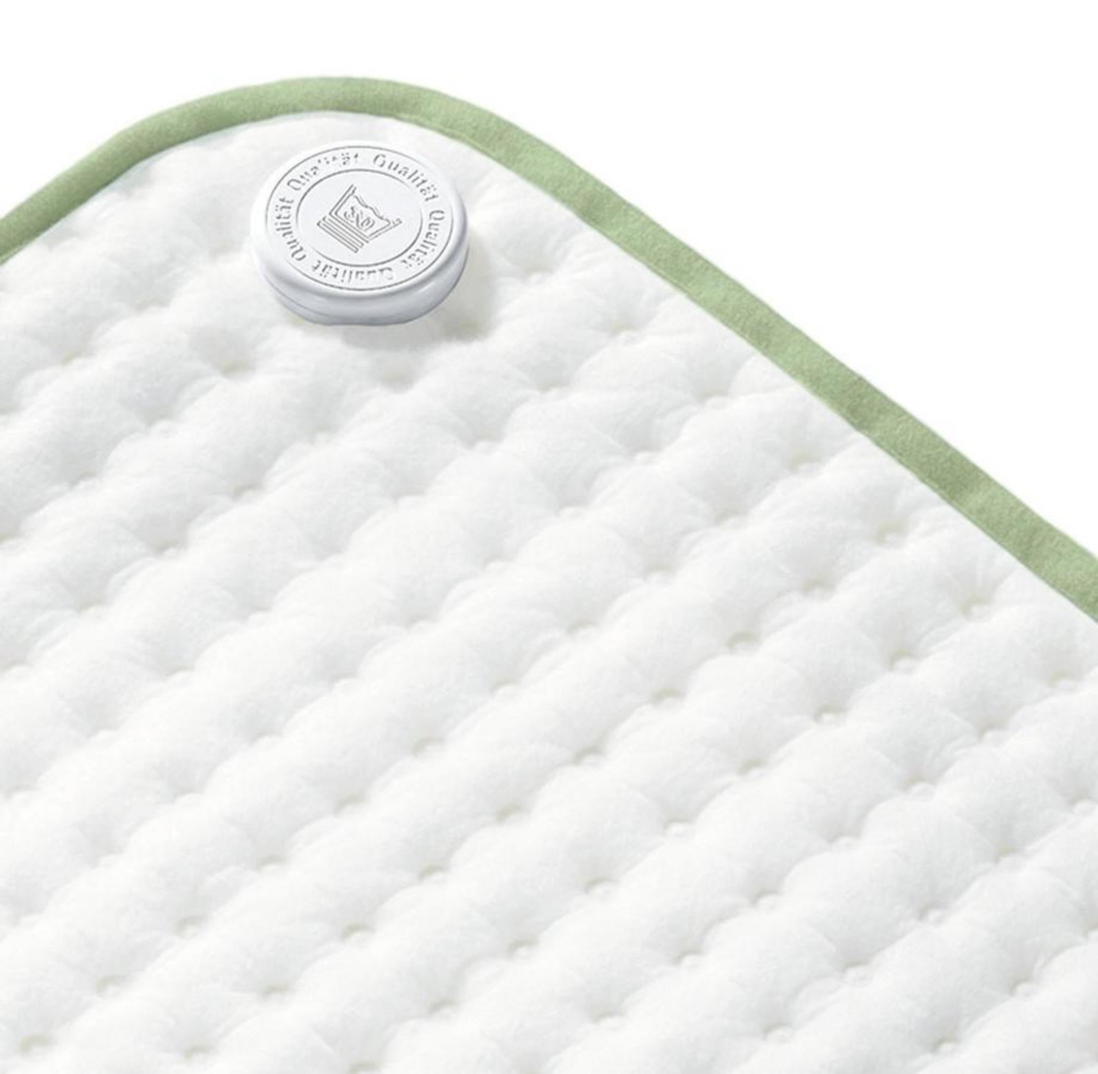 Primer plano de una manta blanca acolchada con borde verde y etiqueta redonda.