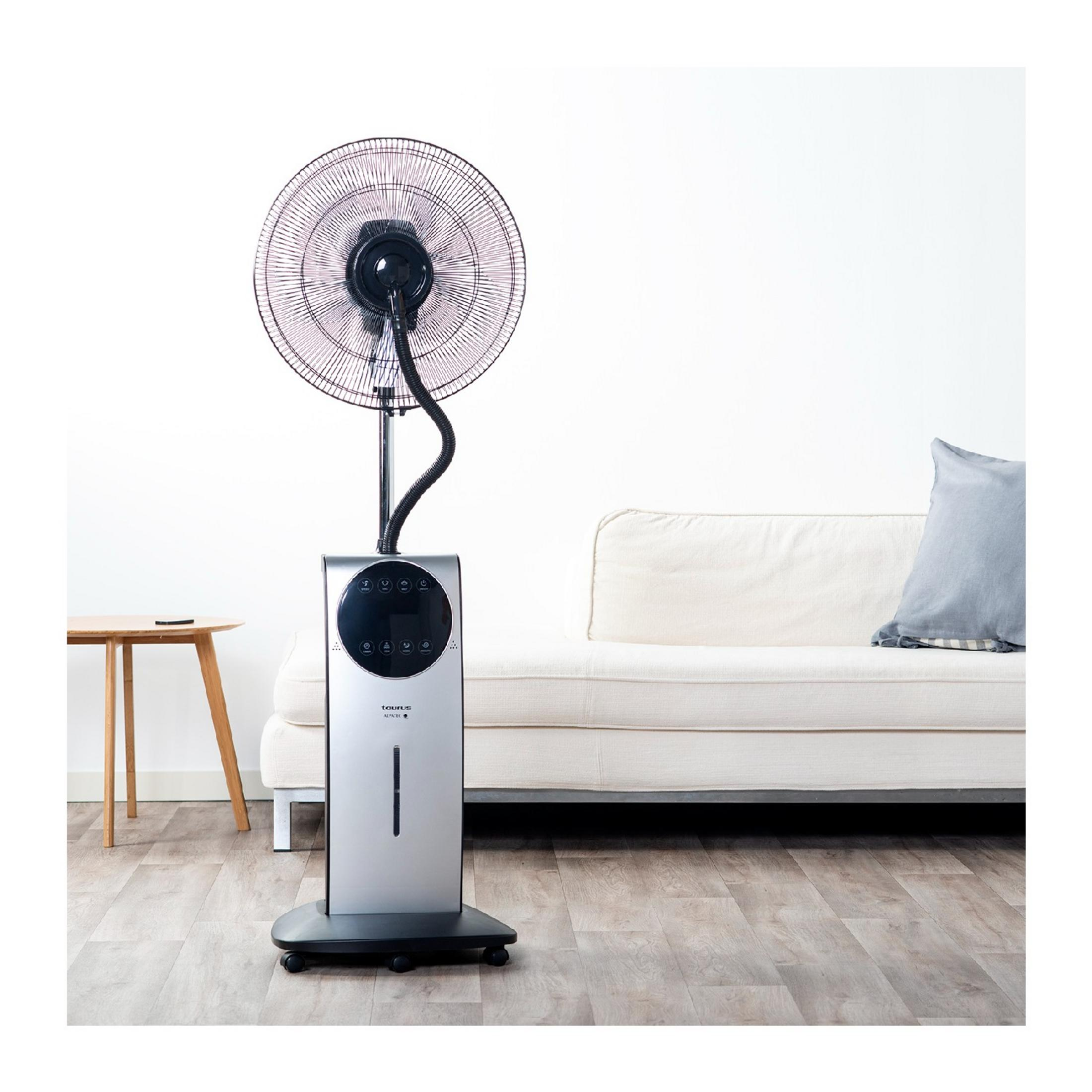 Un ventilador plateado de pie con función de niebla está junto a un sofá.
