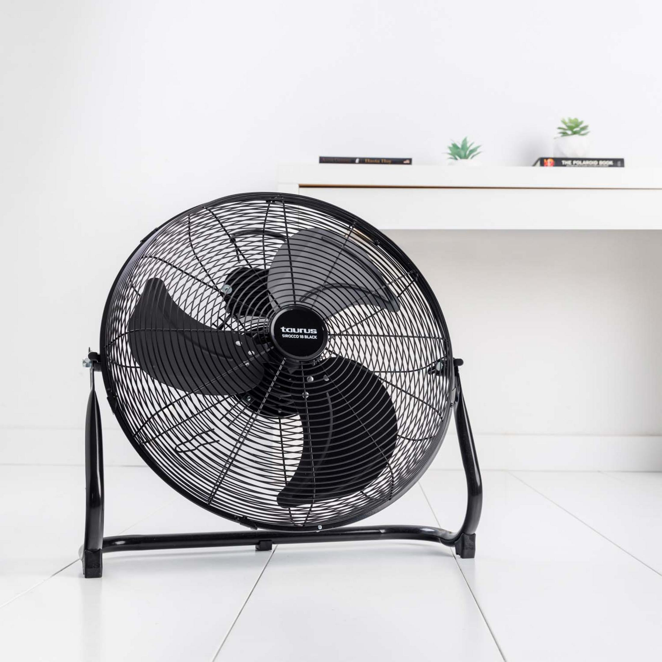Un ventilatore da terra nero con griglia metallica su pavimento in legno bianco.