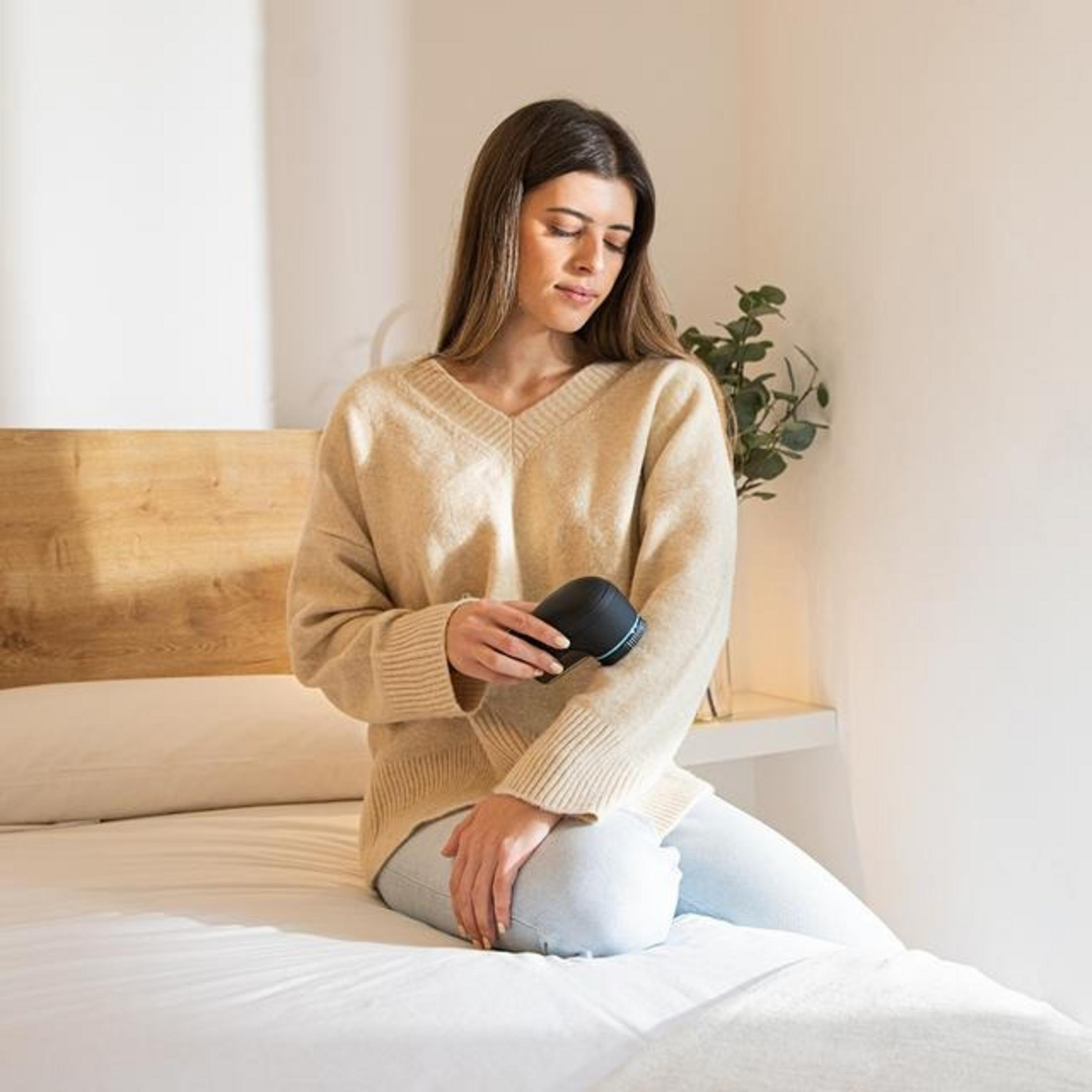 Una donna seduta su un letto usa un piccolo dispositivo nero sul braccio.